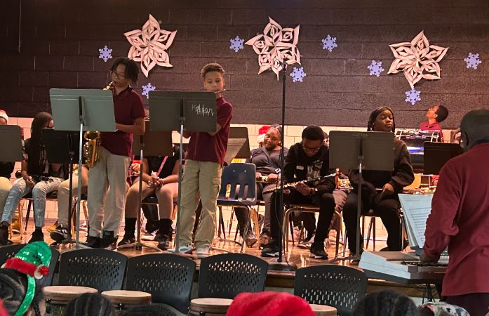 2 students on stage playing instruments with the band sitting behind them
