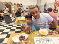 Father and son sitting at a cafeteria table with donuts and coloring sheets