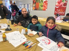 Father and children sitting at a cafeteria table with donuts and coloring sheets