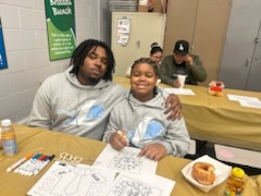 Father and son sitting at a cafeteria table with donuts and coloring sheets