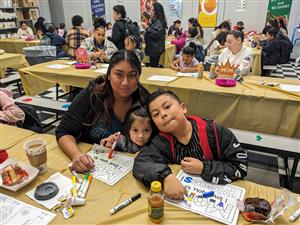 mother and children sitting at a cafeteria table with donuts and coloring sheets