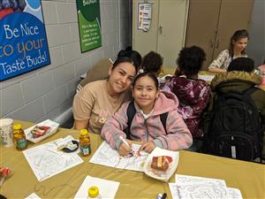 mother and daughter sitting at a cafeteria table with donuts and coloring sheets