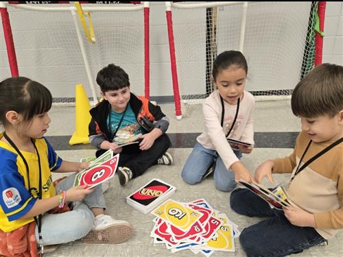 4 kids sitting on a gym floor playing a card game