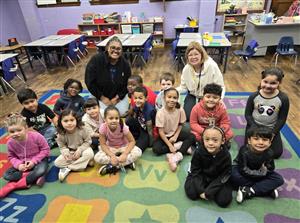 Large group of students and 2 teachers sitting on a rug