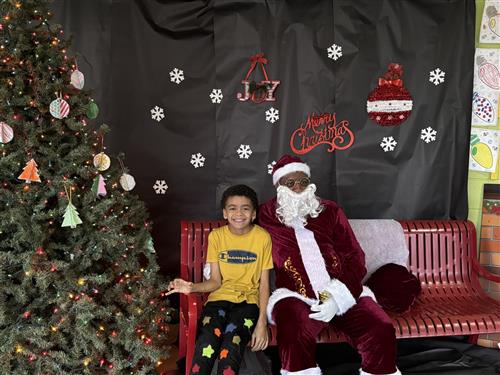 Student taking picture with Santa on red bench next to a Christmas Tree in school hallway