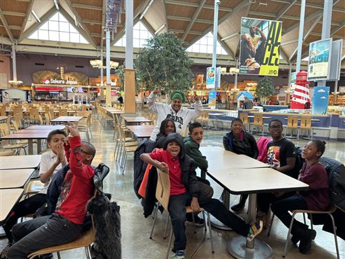 Students and teacher sitting on a mall food court posing for pictures