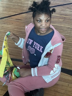 Student sitting on gym floor at pep rally with her pom poms and noise maker.