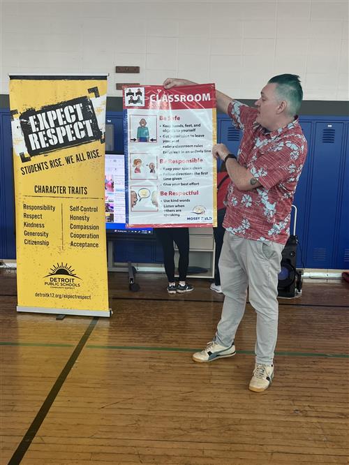 Teacher in school gym at a pep rally discussing what P.B.I.S. is with students