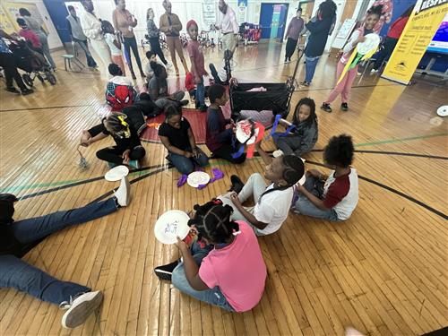Students sitting on gym floor preparing for pep rally with pom poms and noise makers.