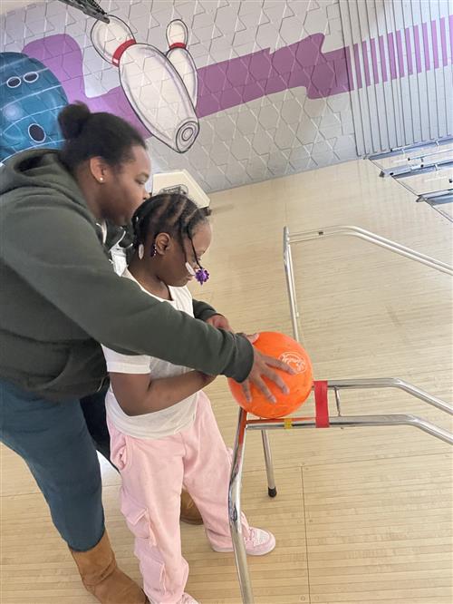 Teacher assisting student using an adaptive ramp to bowl at a bowling ally