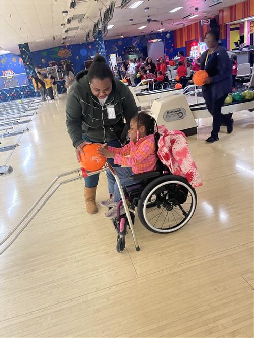 Teacher assisting student using an adaptive ramp to bowl at a bowling ally