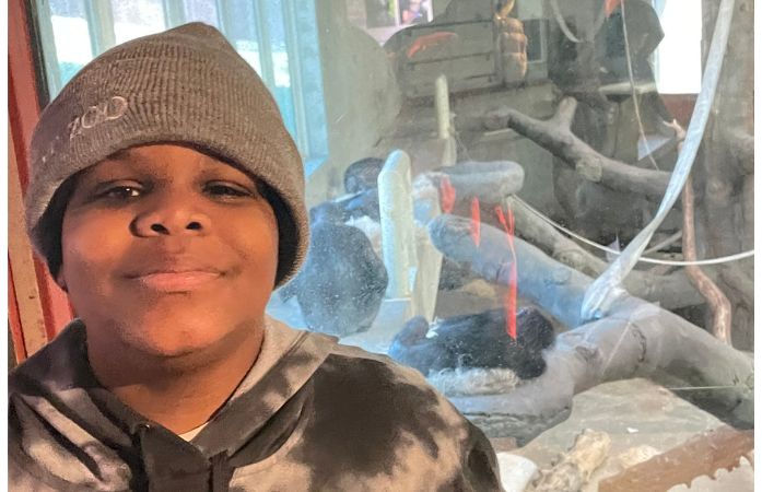  6th grade student smiling in front of ape enclosure at Detroit Zoo. 