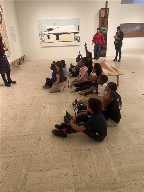 students sitting in front of artwork while a museum worker explains it