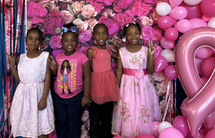  4 smiling girls dressed in pink in front of flower background