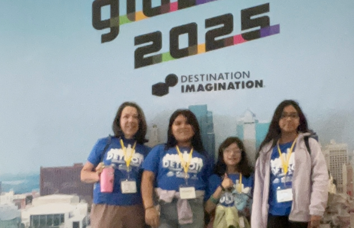  Students and teacher standing  in front of Destination Imagination Global sign