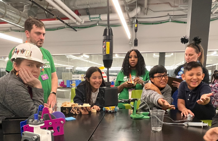  Students and mentors working on their robotics projects and smiling