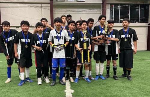 A group of boys in their soccer uniform, holding trophies.