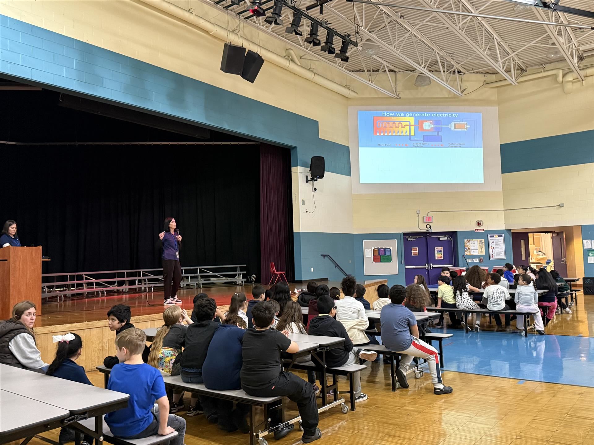adult presenting on the stage while students sit and watch