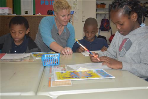 Volunteer from Tutormate sits with 3 first grade students 