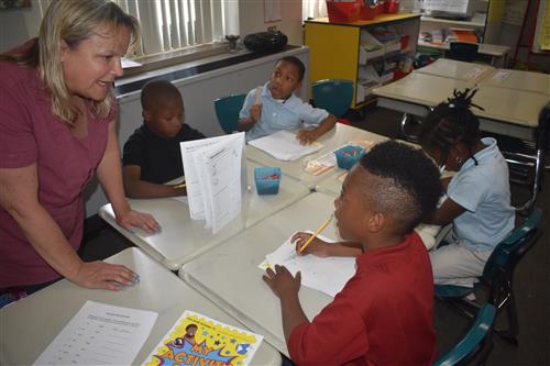 Tutormate volunteer stands while talking to first grade students 