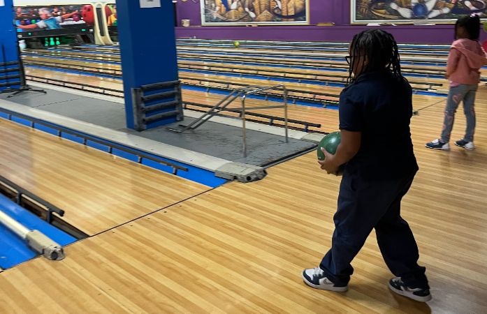  A student approaching a bowling lane while holding a bowling ball.