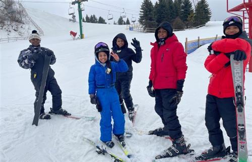  5 students in ski gear and ski posing on the slopes