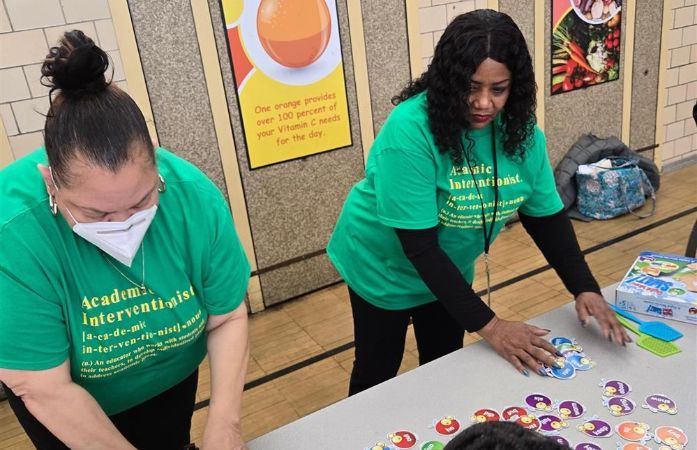   Two women wearing green shirts play a game on a table.