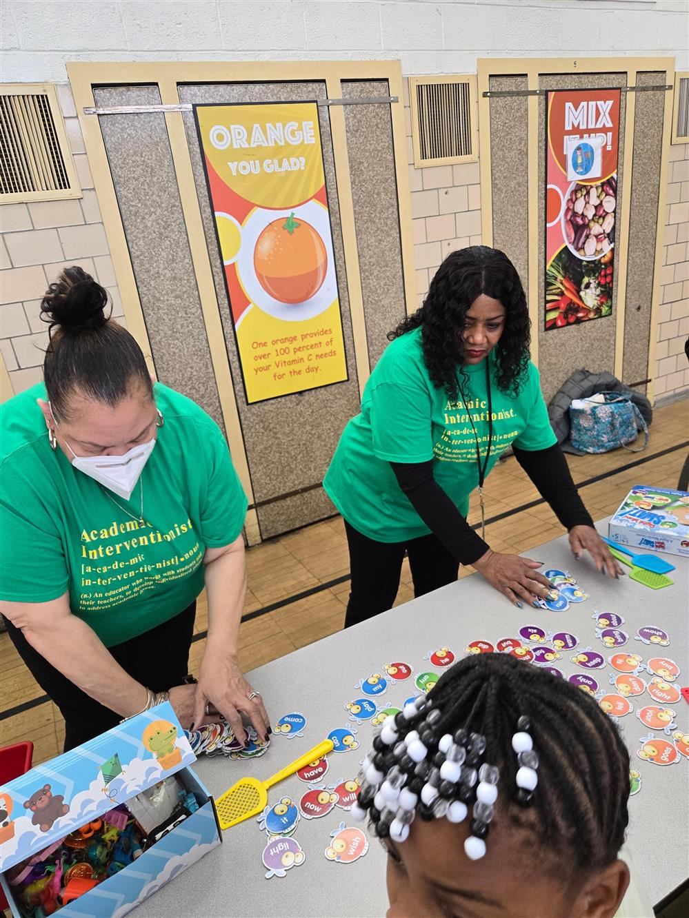  Two women wearing green shirts play a game on a table.