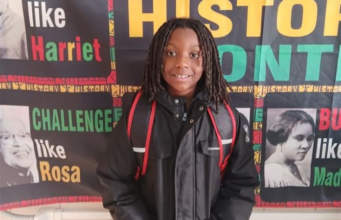   Little boy standing in front of a black history month banner.