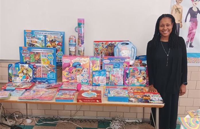   A woman stand next to a table with books.