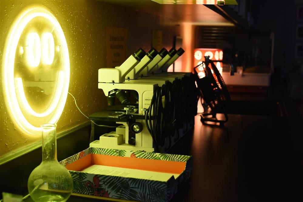  Picture of a neon smiley face backdropped by lab microscopes.