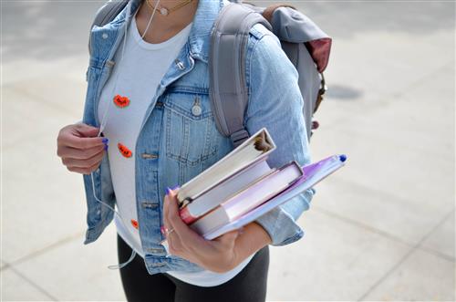 Student holding books, wearing earbuds and wearing a backpack 