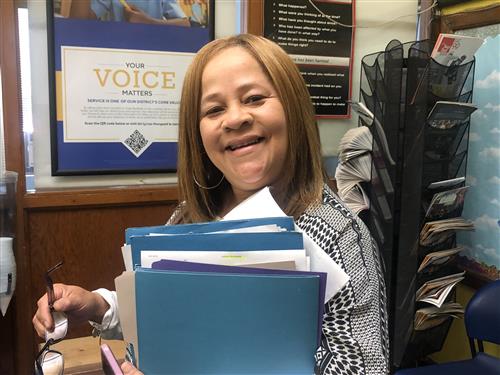 Teacher smiling with blue folders wearing a black and white blouse