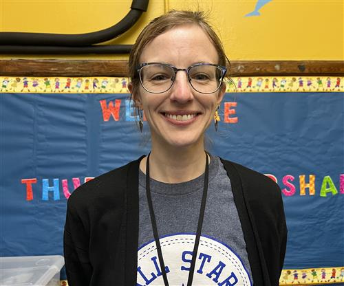 Ms. Wellom smiling with glasses. She is wearing a black and blue shirt.
