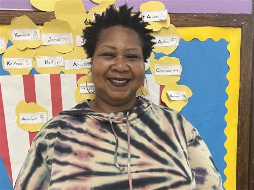 Teacher smiling with a pink, black and cream color blouse.