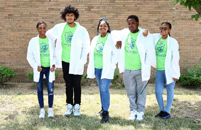  Five students standing together outside wearing lab coats and smiling