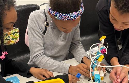 2 girls and a boy putting a Lego robot together
