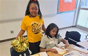  2 girls, one sitting and 1 standing with a cheer uniform on