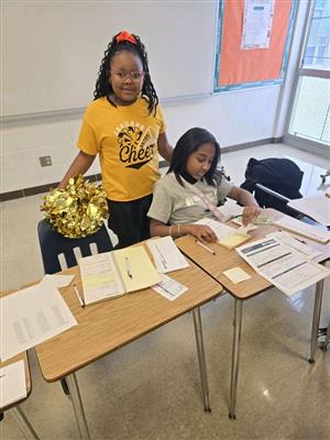 2 girls, one standing with a cheer uniform on and 1 sitting