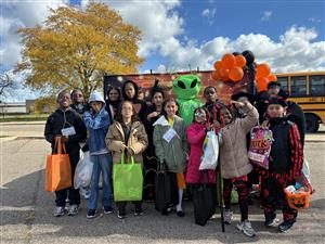  students dressed in different halloween costumes and standing in front of a fall themed background