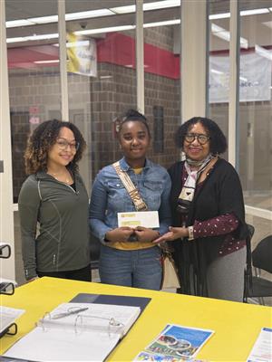  2 women standing beside a student holding an envelope. 