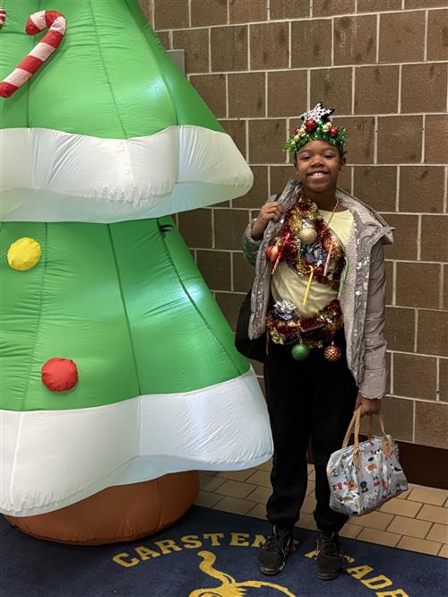 A girl standing next to a holiday prop smiling while dressed in holiday gear. 