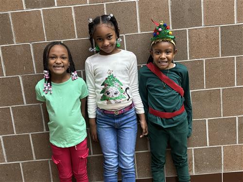 Three young girls smiling for a picture in front of a brick wall. 