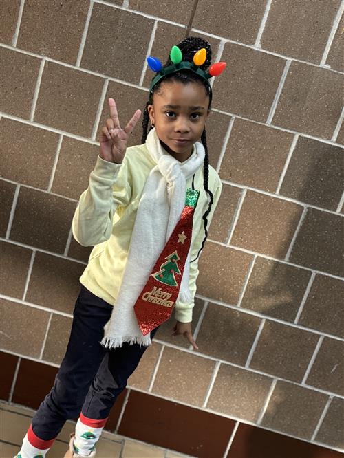 a girl holding the peace sign, standing in front of a brick wall wearing a festive headband and tie to correlate. 