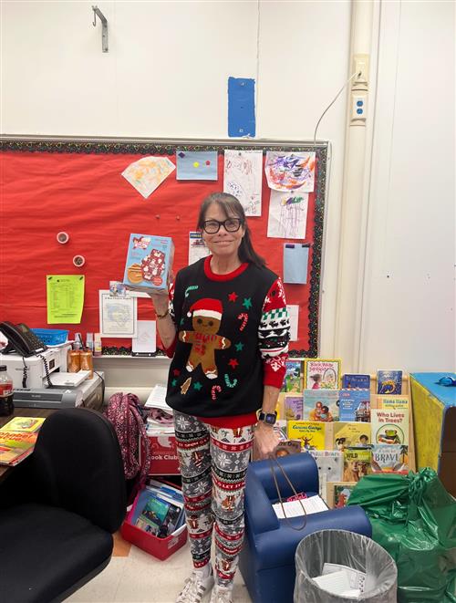 a lady dressed in a holiday sweater posed in front of a classroom bulletin board.