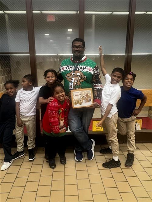 a man dressed in a holiday sweater posed in front of windows, posed with a group of six smiling students.