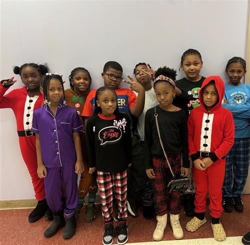 10 students posed together holding up peace signs posed in front of a blue wall, wearing pajamas. 