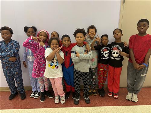 11 students posed in front of a blue wall with different facial expressions wearing pajamas. 