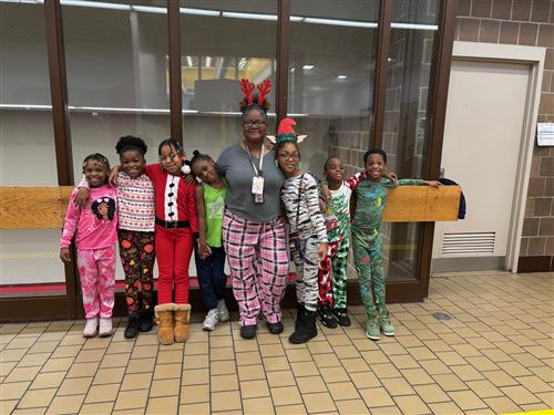 7 students posed in pajamas in front of glass with an adult wearing smiles. 