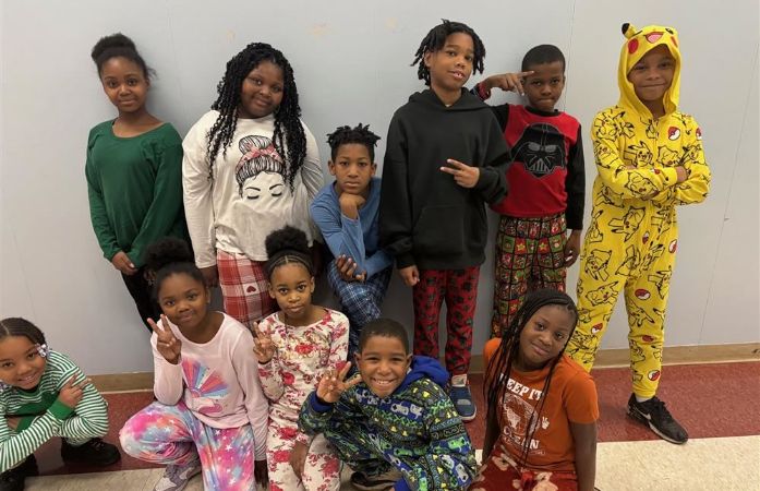   11 Boys and Girls dressed in pajamas and smiling in front of a blue painted wall